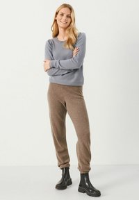 Suéter gris claro con textura de canalé, de manga larga y cuello redondo, combinado con unos pantalones jogger marrones de corte holgado. Botines negros completan el conjunto.