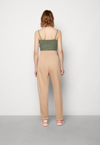 Olivovo zelený crop top s tenkými ramienkami, skombinovaný s béžovými nohavicami s vysokým pásom. Nohavice majú elastický lem na členkoch.