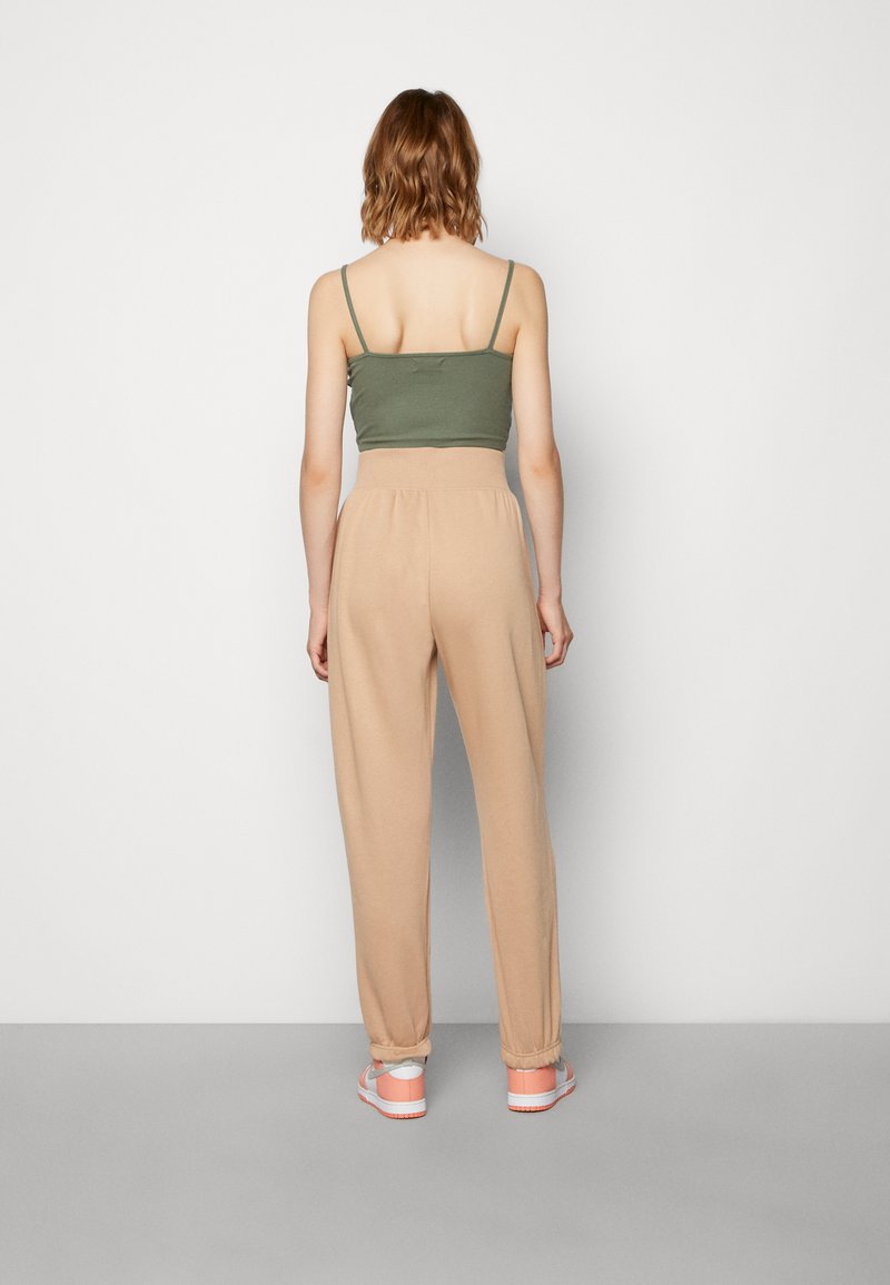 Top corto verde oliva con spalline sottili, abbinato a pantaloni beige a vita alta. I pantaloni hanno un polsino elastico alle caviglie.