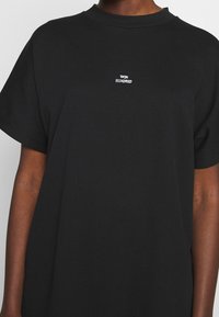 Une personne portant un t-shirt noir avec un petit texte blanc "WON HUNDRED" centré sur la poitrine.