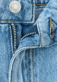 Svetlo modra jeansa tkanina z zadrgo in gumbnim zapiranjem. Opazni šivi v zlati barvi in vidni notranji žep z teksturirano površino.