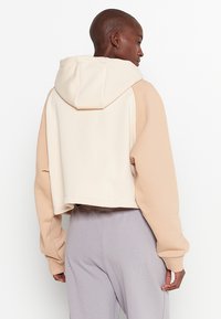 Felpa accorciata con un design a blocchi di colore beige e crema, realizzata in un tessuto morbido. Presenta un cappuccio e maniche lunghe con polsini a costine.