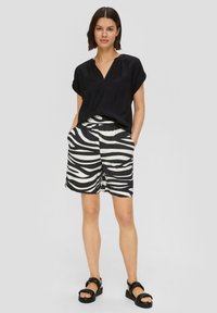 Schwarze Bluse mit kurzem Arm und V-Ausschnitt, kombiniert mit weißen und schwarzen Shorts im Zebra-Druck. Mit elastischem Bund und Seitentaschen.