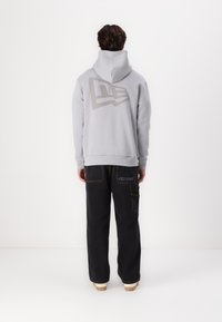 Felpa grigia con un grande logo smorzato sulla schiena, abbinata a pantaloni cargo neri con cuciture decorative e tasche laterali.