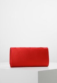 Rode stoffen clutchtas met een rechthoekige vorm, een gladde textuur en horizontale plooien aan de voorkant, geplaatst op een wit voetstuk.