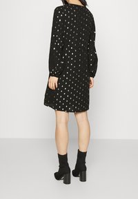 Černé šaty s dlouhými rukávy, zdobené kovovými stříbrnými puntíky, s vypasovaným pasem a kulatým výstřihem. Nosené s černými kotníkovými botami.