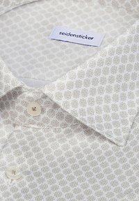 Chemise blanche avec motifs géométriques en forme d'étoile beige, devant à boutons, avec une étiquette "seidensticker" à l'intérieur du col.