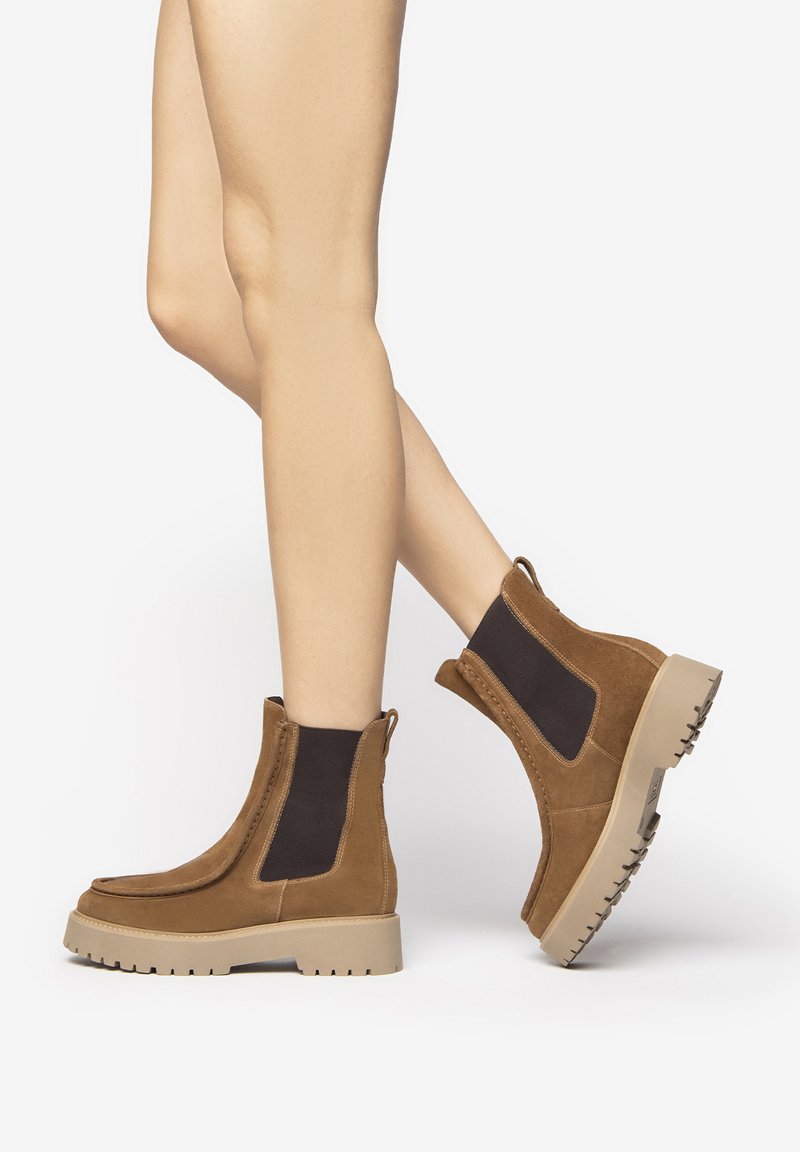 Bottines en daim marron avec des panneaux latéraux en élastique, des semelles en caoutchouc texturé et un design à bout rond.