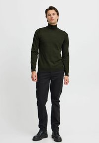 Pull en col roulé vert olive en tissu tricoté, associé à un jean slim noir et des bottes noires à lacets. Design simple, sans motifs.