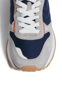 Navy and grey sneaker with suede and textile materials, white laces, orange accent stitching, and a textured rubber sole.