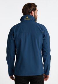Sötétkék softshell dzseki magas gallérral, sárga logóval a hátsó részen és cipzáras oldalzsebekkel. Simaság, valamint testhez álló fazon jellemzi.