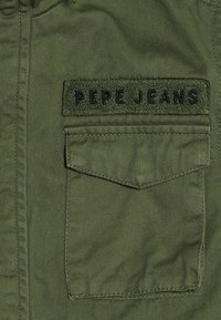 Oliwkowa kurtka z kieszenią z przodu z wyciąganym klapkiem oraz fakturowaną naszywką z napisem "PEPE JEANS" w ciemnych literach.