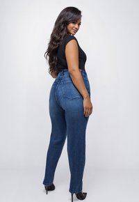 Hoge taille blauwe denim jeans met een slim fit, voorzien van twee achterzakken en een subtiele vervaging, gecombineerd met zwarte hakken en een aansluitend topje.