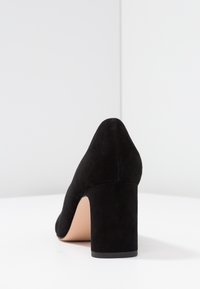 Scarpa nera in suede con tacco alto, punta affilata e tacco robusto, caratterizzata da una texture liscia e un design semplice ed elegante.