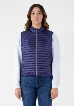 Gilet imbottito blu navy con trapuntatura orizzontale, colletto alto, zip frontale e materiale leggero. Indossato sopra una camicia bianca a maniche lunghe.