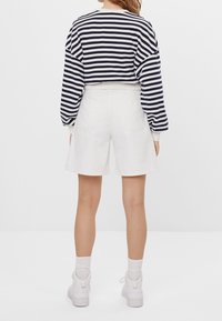 Felpa accorciata a righe navy e bianche con maniche a sbuffo, abbinata a pantaloni bianchi e sneakers bianche. Texture in cotone morbido, vestibilità casual.