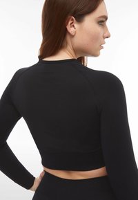 Top corto nero a maniche lunghe con design aderente, tessuto morbido, maniche raglan e orlo a costine. Presenta un discreto logo del brand sul retro.