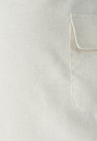 Platno v svetlo bež barvi z vdelano žepom. Tekstura se zdi rahlo groba z naravno, brezhibno končno obdelavo.