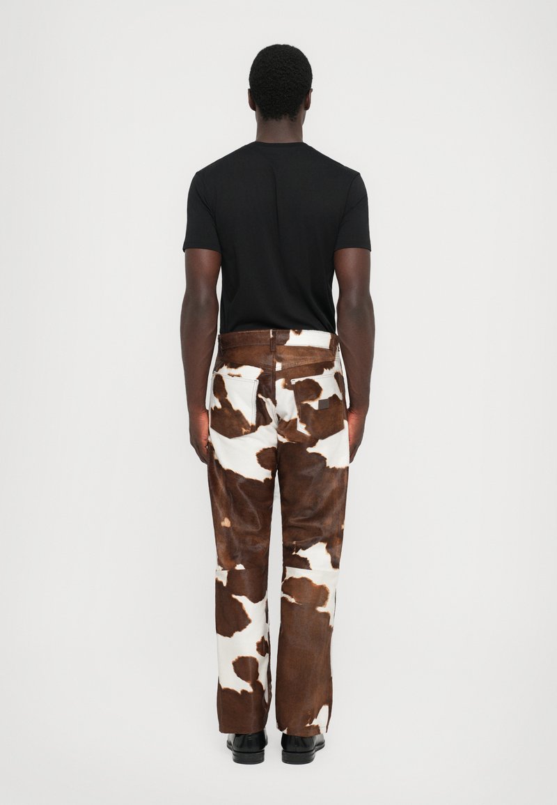 Hosen mit braun-weißer Kuhflecken-Musterung, gerader Schnitt, strukturierten Stoff und einem Fünf-Taschen-Design. Kombiniert mit einem schwarzen, eng anliegenden T-Shirt.