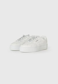 Baskets en cuir blanc avec une semelle en caoutchouc épaisse, un bout rond et un design à lacets. Présente des détails perforés et un logo discret sur le côté.