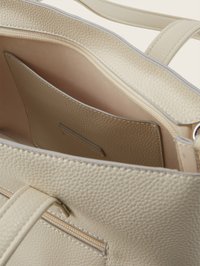 Sac à main en cuir texturé beige clair avec poche zippée, poche intérieure et doubles anses visibles en gros plan.