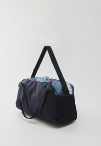 Egy sötétkék szövet sporttáska fekete hálós oldalpanelekkel, dupla fogantyúkkal és kék mintás felső résszel, amely virág- és absztrakt mintákat tartalmaz.