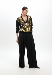 Black sweater with gold circular sequins on the front, V-neck design, paired with tailored black trousers and pointed-toe black shoes.