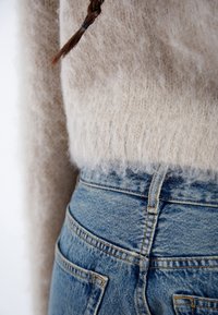 Fuzzy beige sweater with a soft texture paired with light blue denim high-waisted jeans, featuring back pockets and yellow stitching.