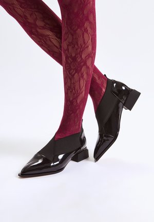 Scarpe in pelle verniciata nera con un design incrociato in elastico, punte appuntite e tacco basso a blocco, abbinate a collant in pizzo bordeaux.
