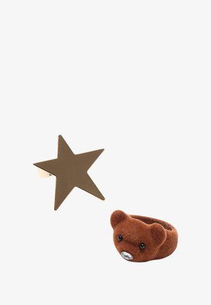 Zlatý prsten ve tvaru hvězdy s lesklým povrchem vedle prstenu ve tvaru hnědého medvěda vyrobeného z měkkého filcu, se černýma očima a nosíkem osázeným rhinestony.