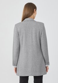 Blazer grigio in felpa con un design aderente, maniche lunghe e un dettaglio a righe nei polsini, che mette in mostra una texture liscia e una silhouette sartoriale.