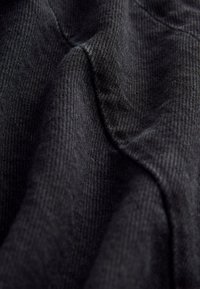 Svart tyg med texturerad väv, som har subtila vågor och en slät yta. Materialet verkar mjukt och något elastiskt.