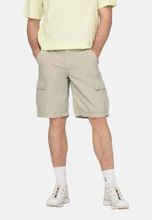 Beige Cargo-Shorts aus leichtem Stoff, mit zwei Seitentaschen und gerader Beinform. Getragen mit einem hellgelben Shirt und weißen Sneakers.