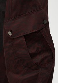 Ciemnoczerwony i czarny materiał w zwierzęcy wzór z klapkową kieszenią zabezpieczoną dwoma metalowymi guzikami z wygrawerowanym napisem "PINKO".