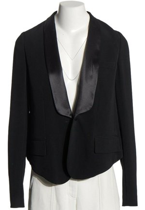 Blazer noir sur mesure avec revers en satin exposé sur un buste de mannequin blanc avec un pantalon blanc.