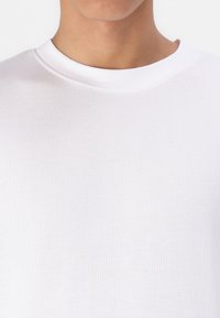 Λευκό βαμβακερό T-shirt με ριγωτό στρογγυλό λαιμό. Το ύφασμα έχει λεία υφή και διακριτική ελαστικότητα, προσφέροντας έναν απλό, μινιμαλιστικό σχεδιασμό.