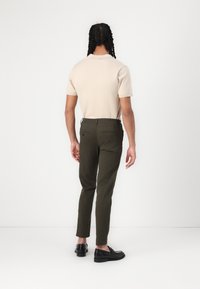Polo shirt beige à manches courtes associé à un pantalon slim fit vert olive et des mocassins noirs, vu de dos.