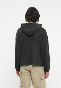 Hoodie oversize gris foncé avec une capuche doublée, épaules basses et ourlet brut. Assorti à un pantalon cargo beige, avec de nombreuses poches.