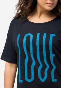 Camiseta de color azul marino hecha de tela suave con la palabra "AMOR" en letras turquesa onduladas y en negrita. Manga corta, cuello redondo.