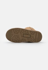 Botte en daim marron avec une semelle en caoutchouc texturée à motif flocon de neige. Présente un design plat et un accent rectangulaire sur la semelle.