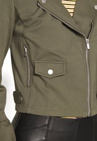 Olive green cropped jacket with zippered closure, side pocket, and snap button detail. Pairing with a black leather bottom.