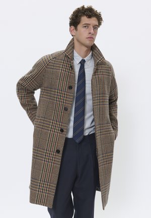 Abrigo de mezcla de lana con un patrón de cuadros en marrón, beige y azul, que presenta un cuello, cierre de botón y un corte relajado. Combinado con una camisa a rayas y corbata.