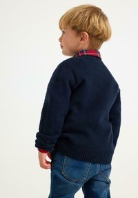 Granatowy dzianinowy sweter z podwiniętymi rękawami, z prążkowanym wykończeniem, noszony na czerwonej koszuli w kratę, zestawiony z niebieskimi dżinsami.