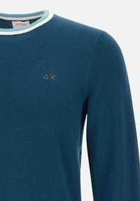 Camicia azzurra in cotone a maniche lunghe con scollatura a coste bianca. Presenta un piccolo logo arancione sul lato sinistro anteriore. Tessuto liscio, design casual.