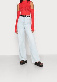 Red long-sleeve top with open shoulders, featuring a textured design. Light blue wide-leg jeans with a high waist, paired with black platform sandals.