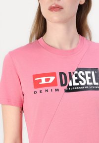 Pink cotton t-shirt with a round neckline, featuring a black and red graphic logo reading "DIESEL DENIM" and "SUCCESSFUL LIVING."