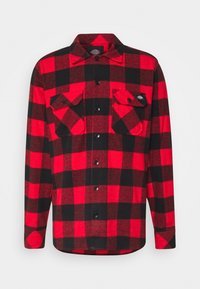 Camisa de franela con cuadros rojos y negros, mangas largas, dos bolsillos en el pecho y cierre de botones en la parte frontal. Tejido suave y texturizado con dobladillo redondeado.