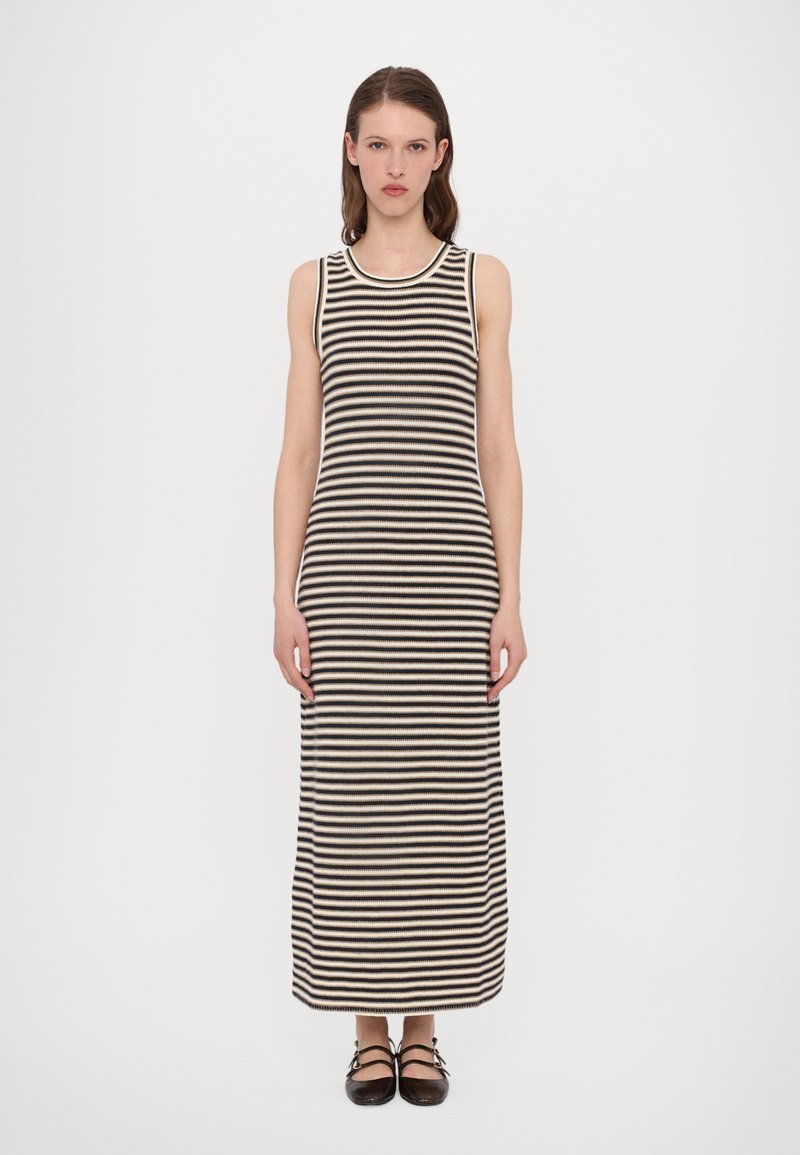 Abito maxi a righe nere e crema con design senza maniche, texture a coste e scollatura rotonda. Le calzature presentano dettagli incrociati.