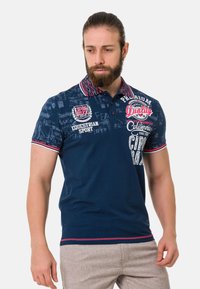 Dunkelblaues Poloshirt aus Baumwolle mit einem gemusterten Kragen, gestickten Akzenten und kontrastierenden gestreiften Abschlüssen an Ärmeln und Saum.