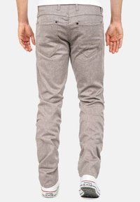 Lichtgrijze, gestructureerde slim-fit broeken met achterzakken en metaalaccenten, gedragen met witte sneakers met blauwe en rode details.